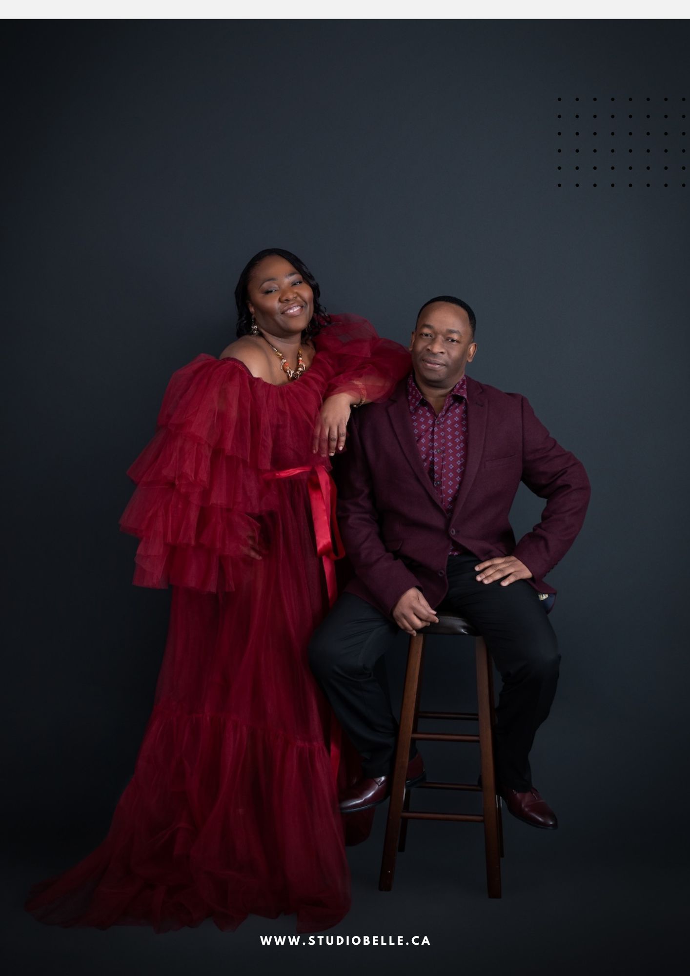 Couple posing in a studio: woman in a voluminous red gown leans on a man in a burgundy blazer against a dark backdrop, with the website bottom text visible.
