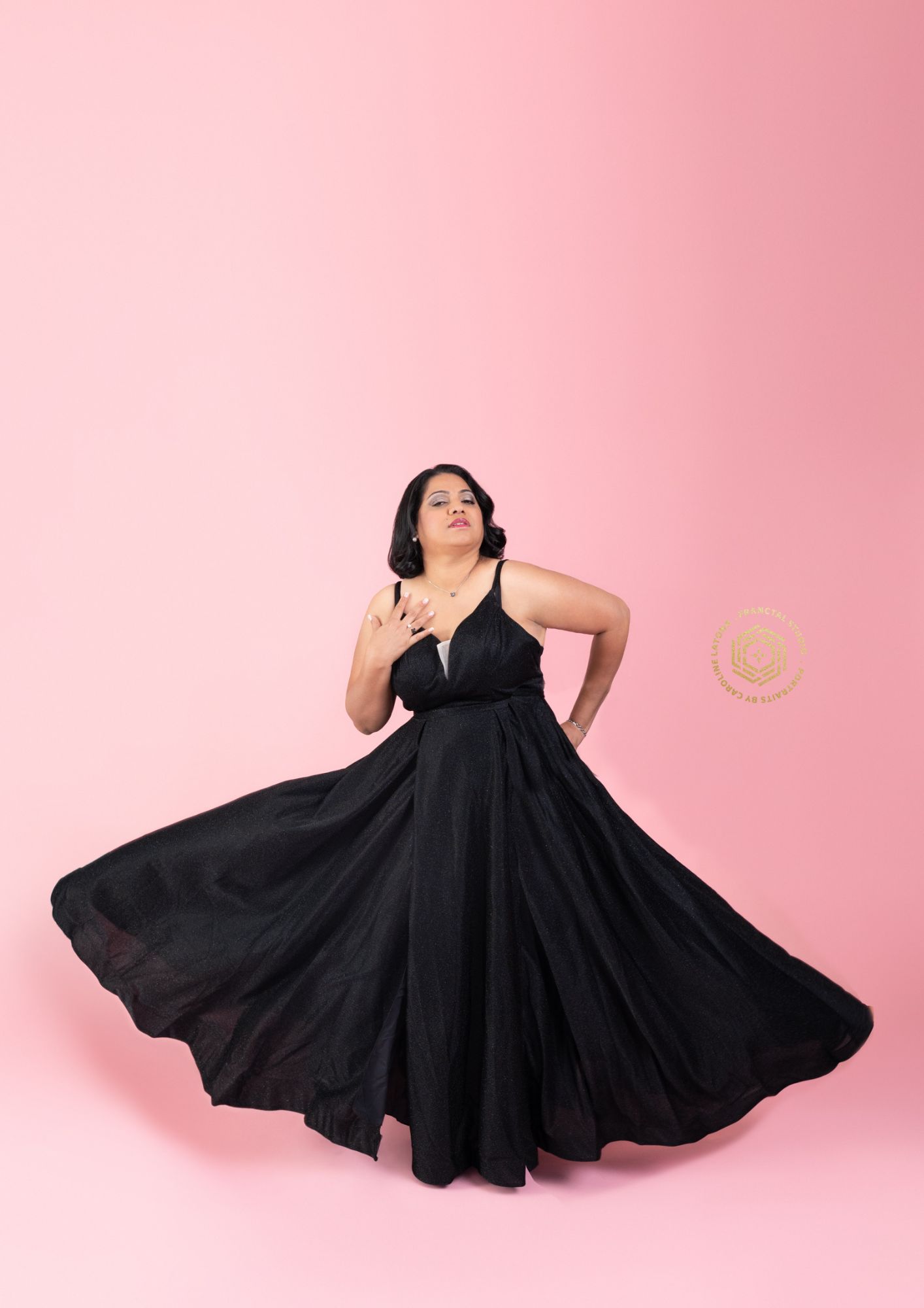 Woman in a flowing black gown whirling against a pink backdrop, mid-dance motion.